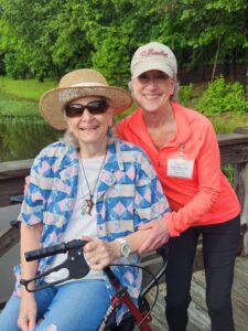 TWO SENIOR LADIES ON  A DOCK WITH GREEN TREES BEHIND
