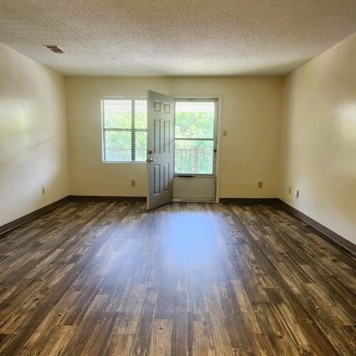 Empty living room with laminate wood flooring, screen door and window at far end of room
